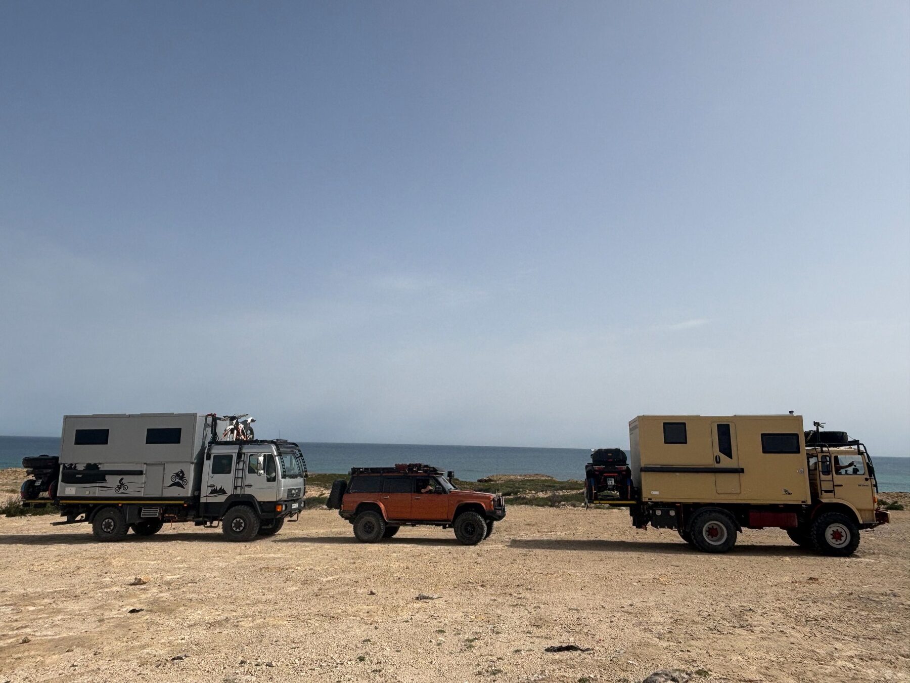 Three Adventure Truck expedition vehicles beside the coast